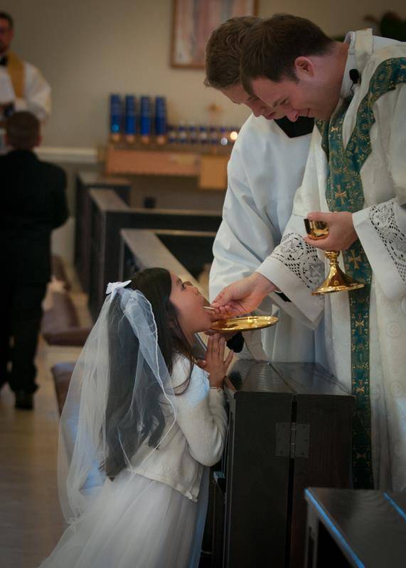 SALISBURY — Josephina Huynh receives her first Holy Communion from Father John Eckert, pastor, during Mass at Sacred Heart Church May 6. Also pictured is the entire class of first Communicants at the parish. (Photos by Bill Washington | Catholic News Hera